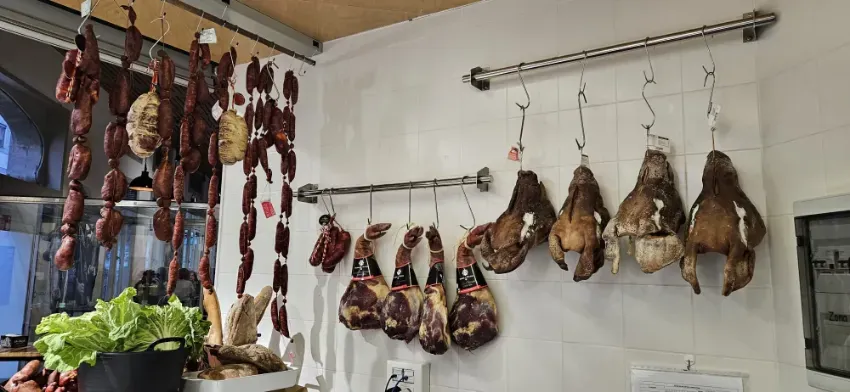 Pescado curado y carnes ahumadas con forma de pez colgando de varillas de metal en un puesto del mercado.