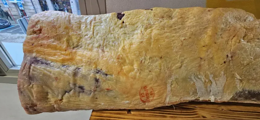 Gran losa de mineral o roca de color amarillo pálido con vetas marrones y moradas, que reposa sobre una superficie de madera.
