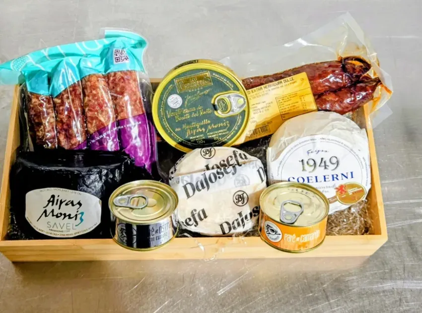 Surtido de productos gourmet y quesos dispuestos en una bandeja de madera con envase transparente.