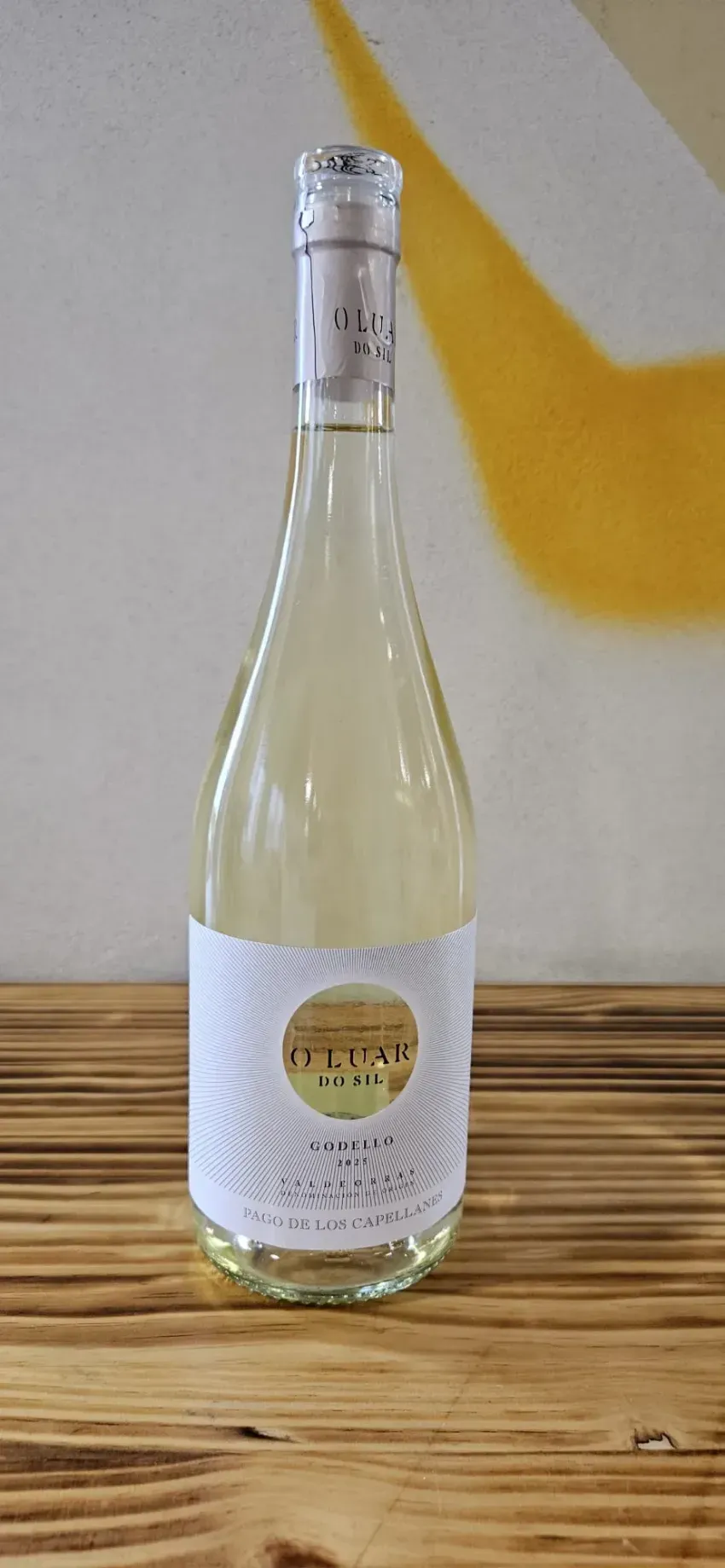 Botella de vino de vidrio transparente con etiqueta blanca colocada sobre una superficie de madera contra un fondo claro.