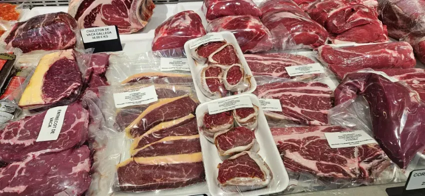 Variedad de cortes de carne de res cruda expuestos en una vitrina de carnicería, con bandejas envueltas en plástico y etiquetas.
