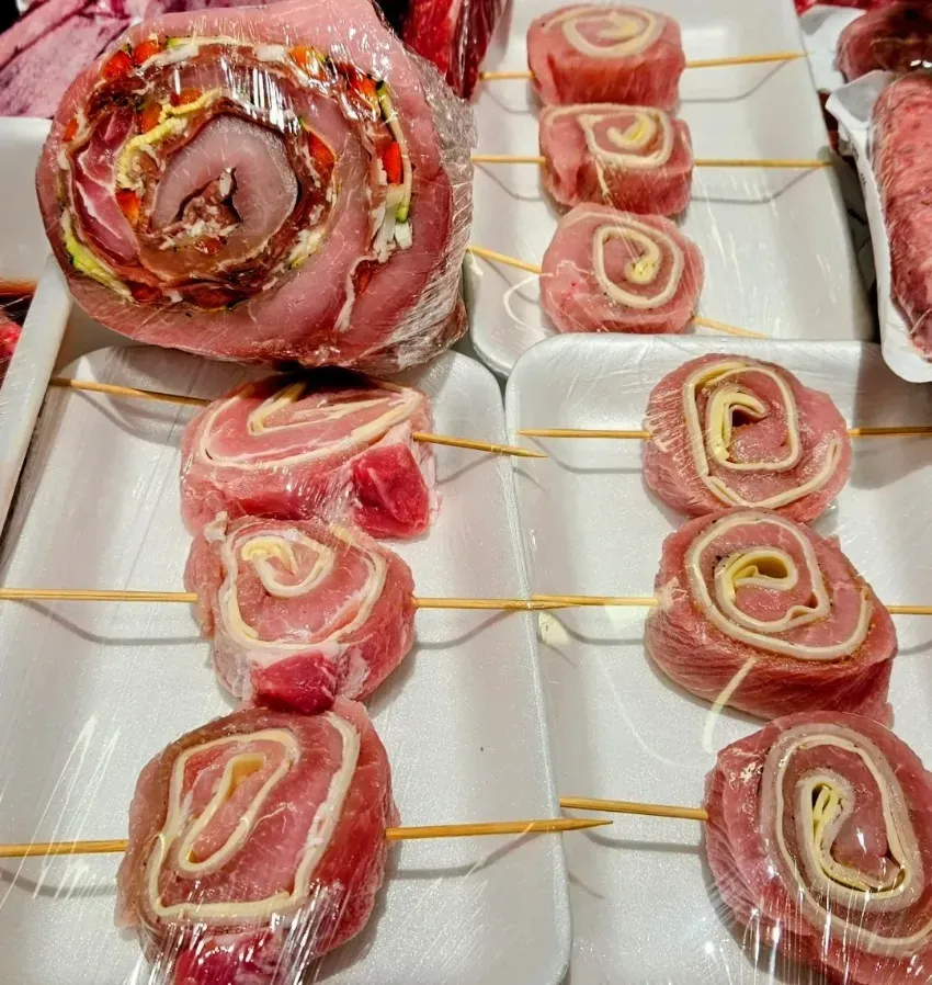 Bandeja con panecillos crudos envueltos en tocino, ensartados en brochetas y dispuestos en filas ordenadas sobre una fuente blanca.