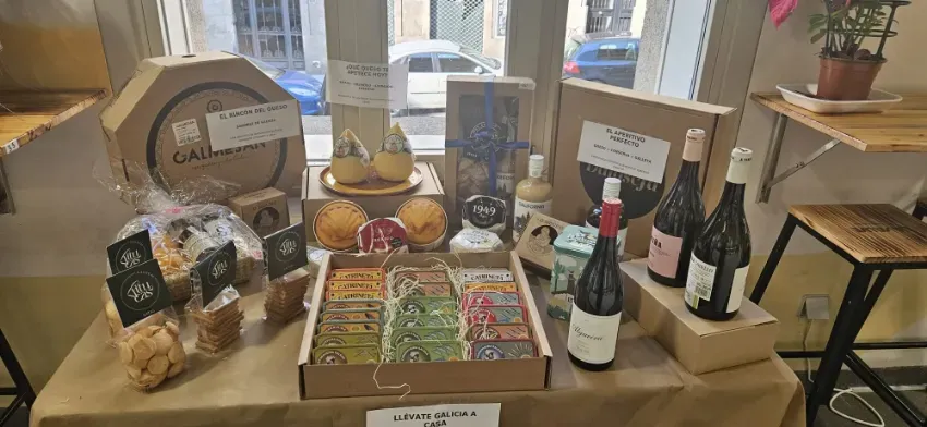 Exhibición de botellas de vino, ruedas de queso y alimentos envasados sobre una mesa en un puesto de mercado rústico.