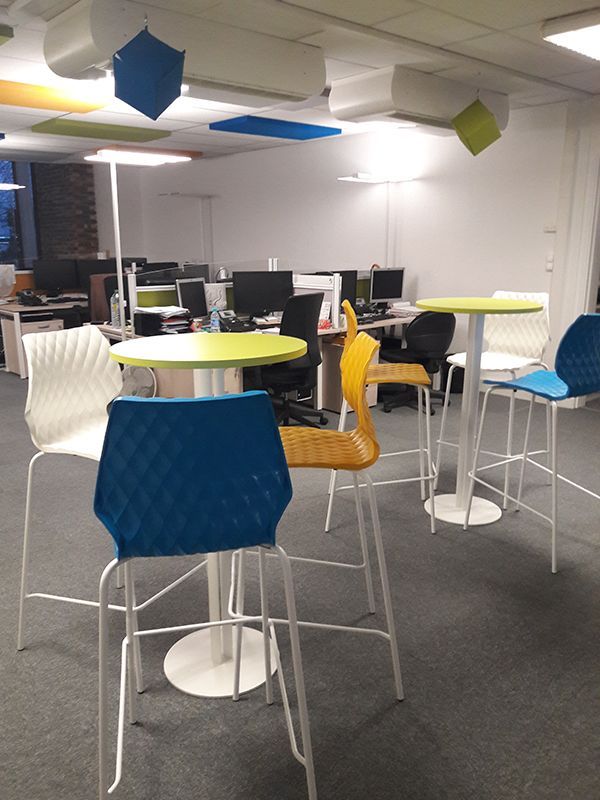 Vue d'un open-space depuis des petites tables rondes avec 3 chaises hautes et des benchs 4 places en arrière-plan