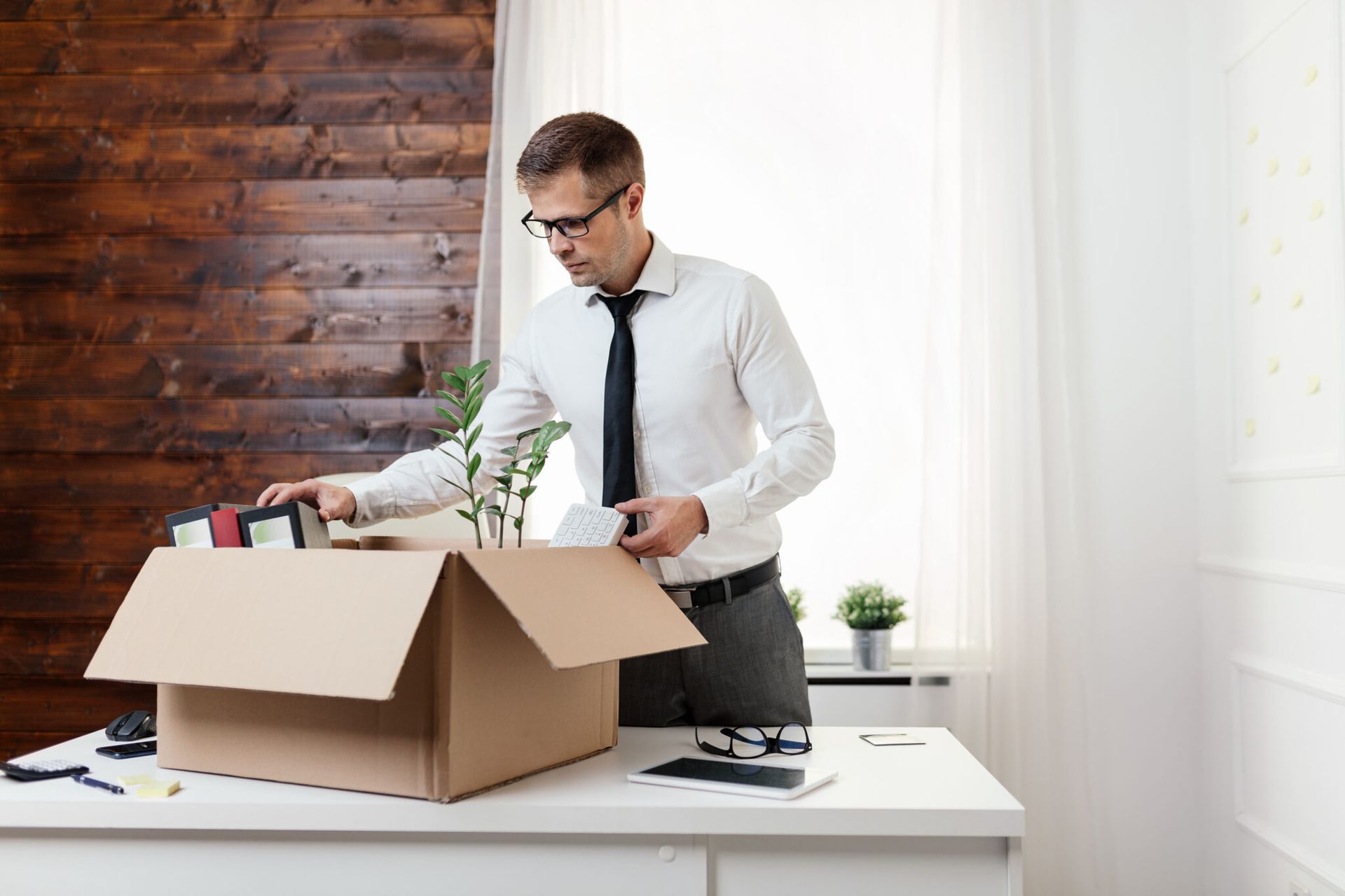 Un homme en chemise cravatte qui porte des lunettes fait son carton de déménagement de bureau
