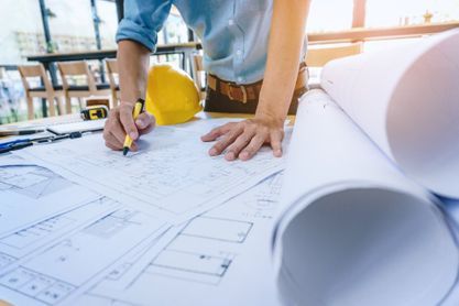 Mann zeichnet etwas in einen Bauplan ein