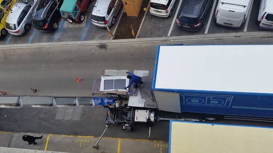 Ein Arbeiter bedient einen Hubwagen, um ein gerahmtes Solarpanel von einem geparkten blauen Lastwagen in der Nähe eines gepflasterten Parkplatzes zu heben.