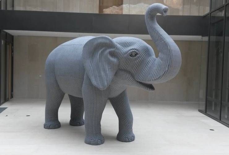 Eine grosse, graue, strukturierte Skulptur eines Elefanten, der mit erhobenem Rüssel in einem Innenhof steht.