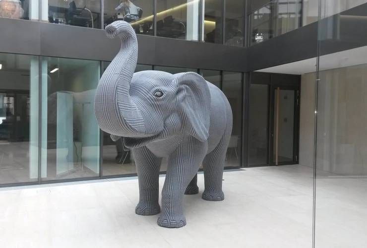 Eine lebensgrosse graue LEGO-Elefantenstatue steht in einem modernen Büroatrium mit Glaswänden.