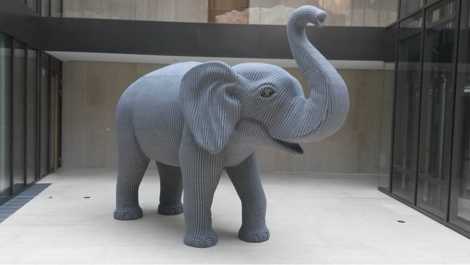 Eine lebensgrosse Elefantenskulptur aus grauen LEGO-Steinen, die mit erhobenem Rüssel in einem modernen Innenhof steht.