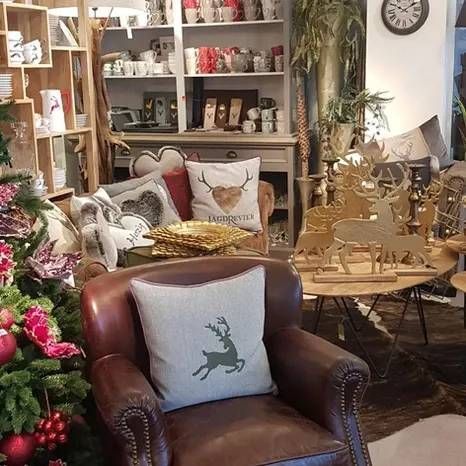 Ein Ledersessel mit einem Rentier-Zierkissen in einem Geschäft mit Weihnachtsdekoration, darunter Regale und goldene Ornamente.