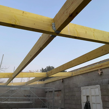 Charpente de toit partiellement construite avec des poutres en bois jaunes au-dessus d'un mur en parpaings et d'un échafaudage.