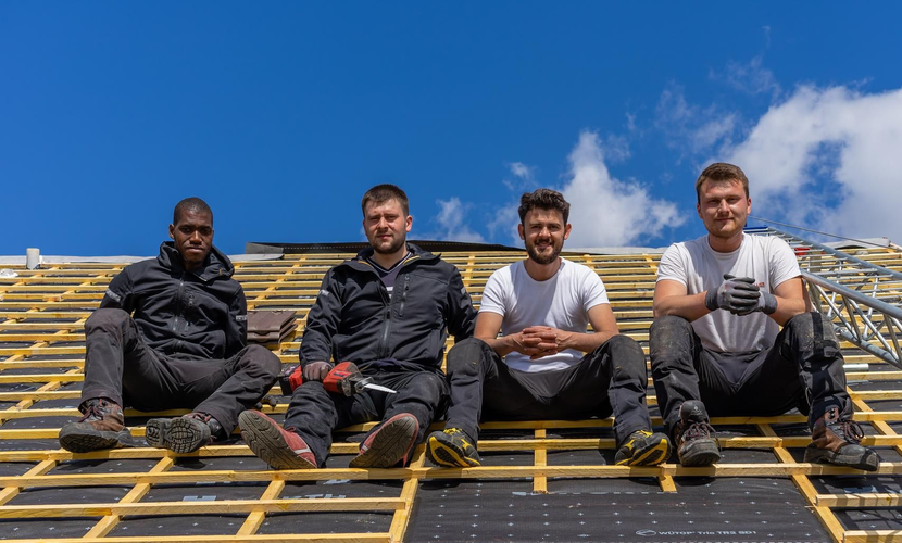 Quatre personnes sont assises sur un toit, sous un ciel bleu.