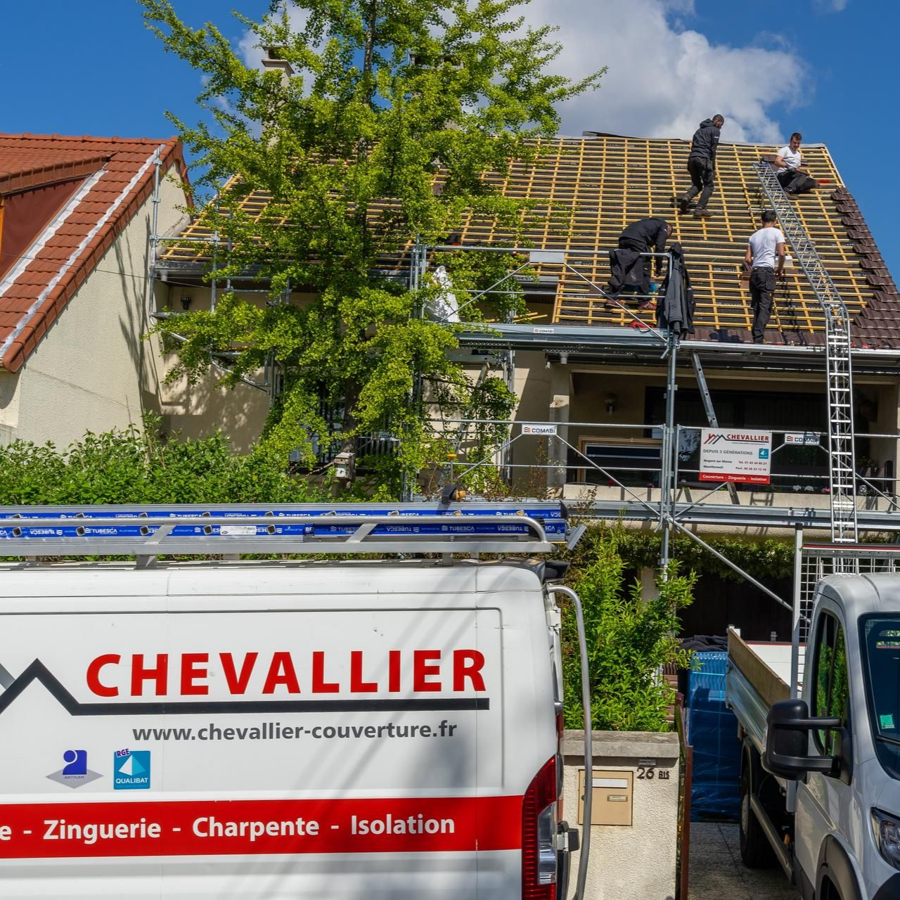Des couvreurs travaillent sur une maison en construction à côté d'un camion de service Chevallier et d'une échelle.
