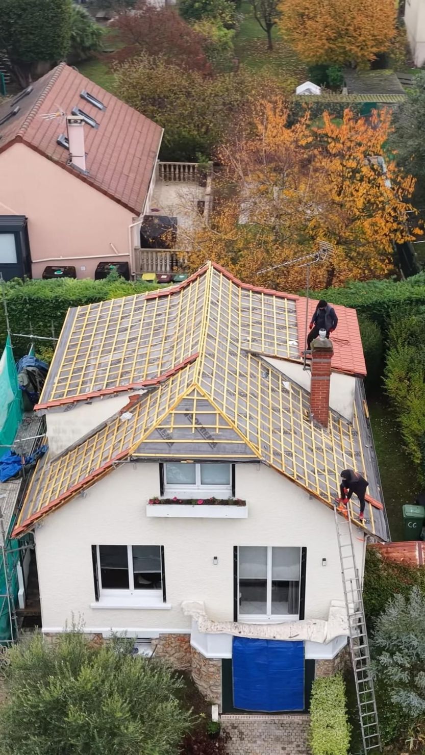 Maison blanche au toit de tuiles rouges abîmé, vue d'en haut parmi les arbres d'automne.