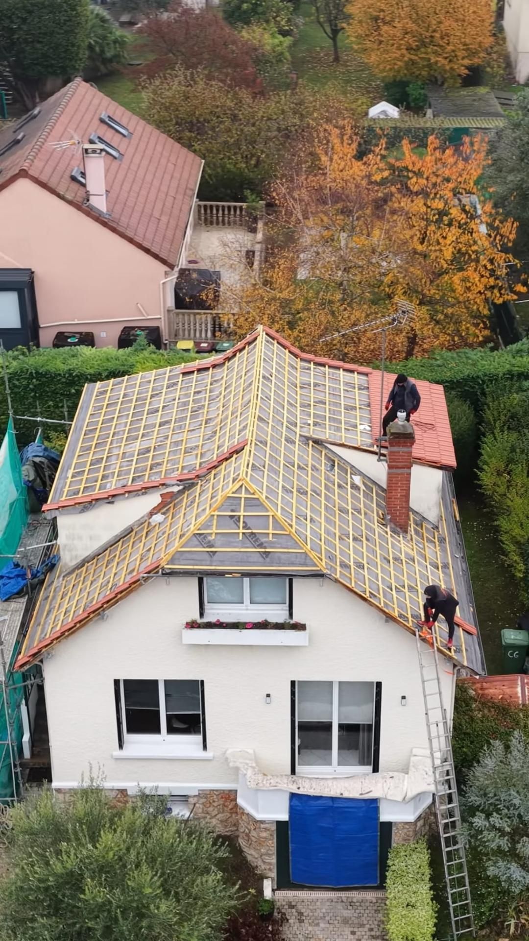 Maison blanche au toit de tuiles rouges abîmé, vue d'en haut parmi les arbres d'automne.