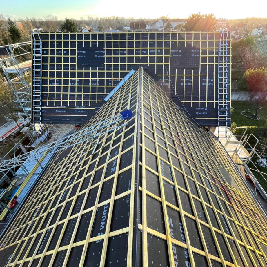 Toit pyramidal quadrillé menant vers un bâtiment sombre en arrière-plan au coucher du soleil.