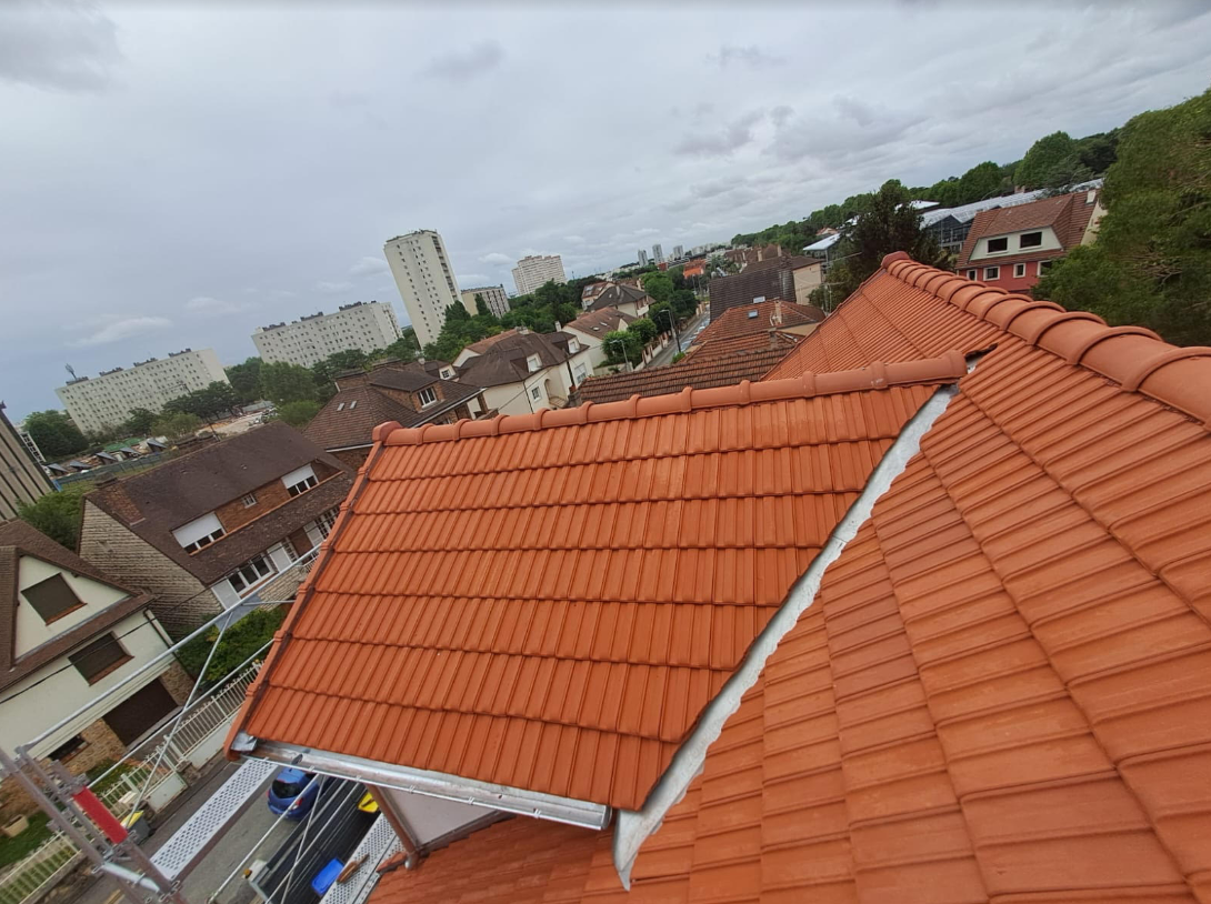 Vue depuis les toits sur des maisons aux tuiles orange et un paysage urbain nuageux.
