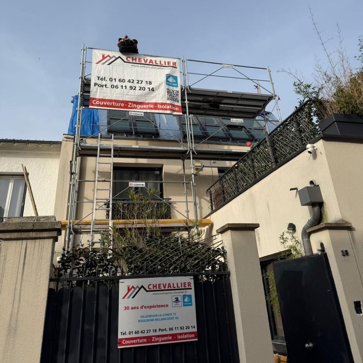 Façade de maison avec échafaudages, panneaux de chantier et entrée fermée par un portail dans une rue résidentielle.