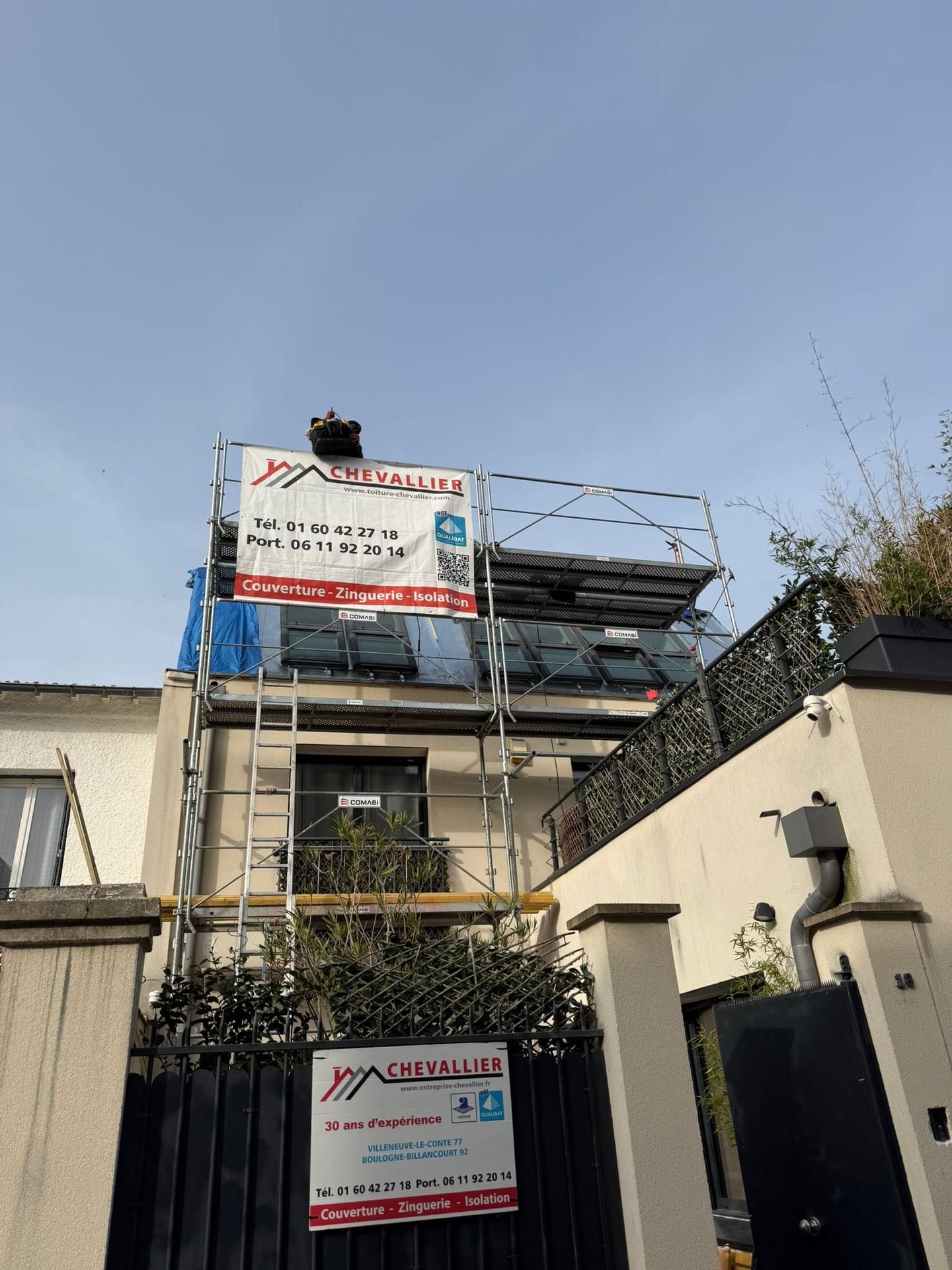 Bâtiment en construction avec échafaudages et portail noir sous un ciel dégagé.