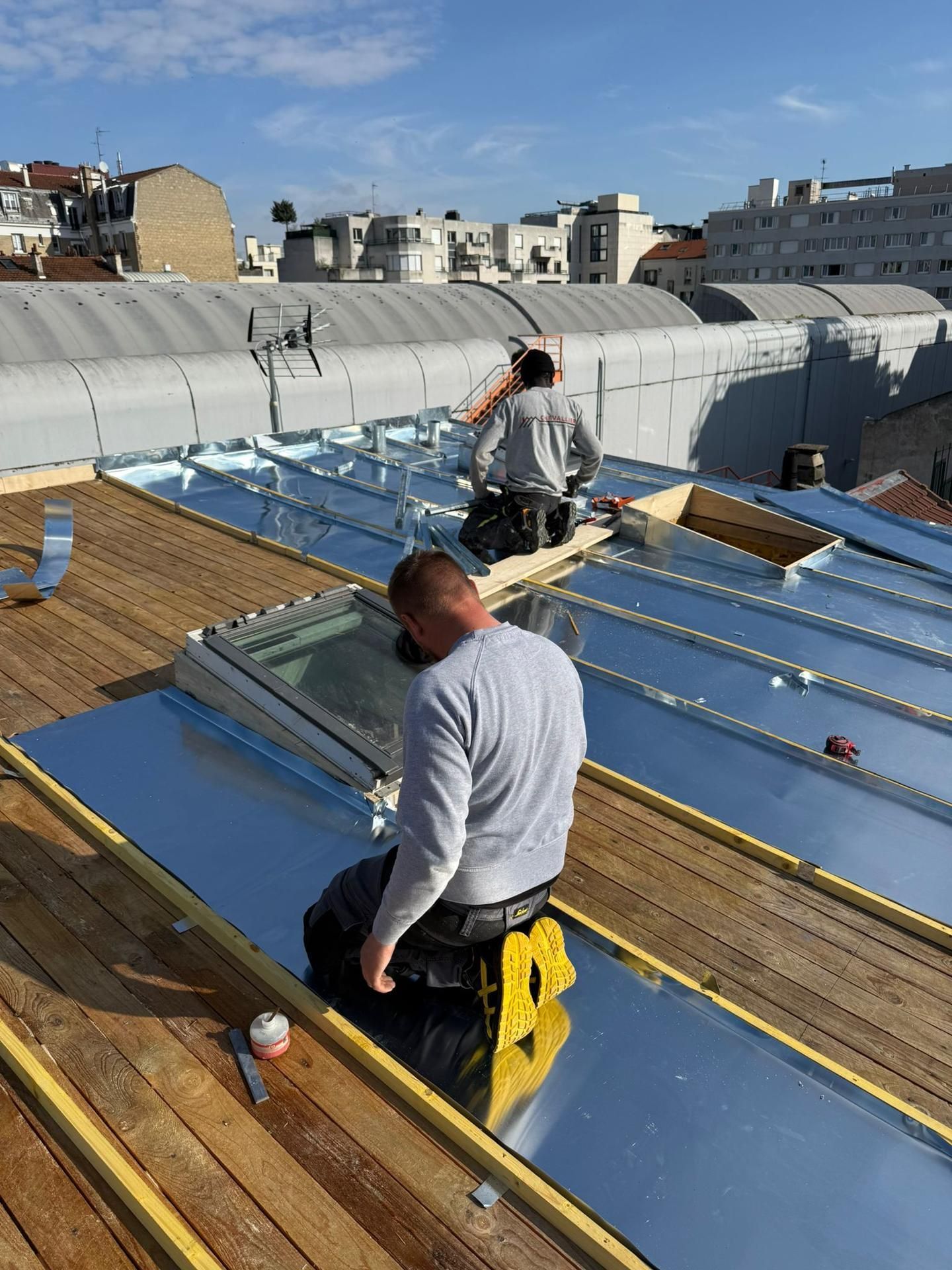 Deux ouvriers installent des panneaux réfléchissants bleus sur un toit sous un ciel dégagé.