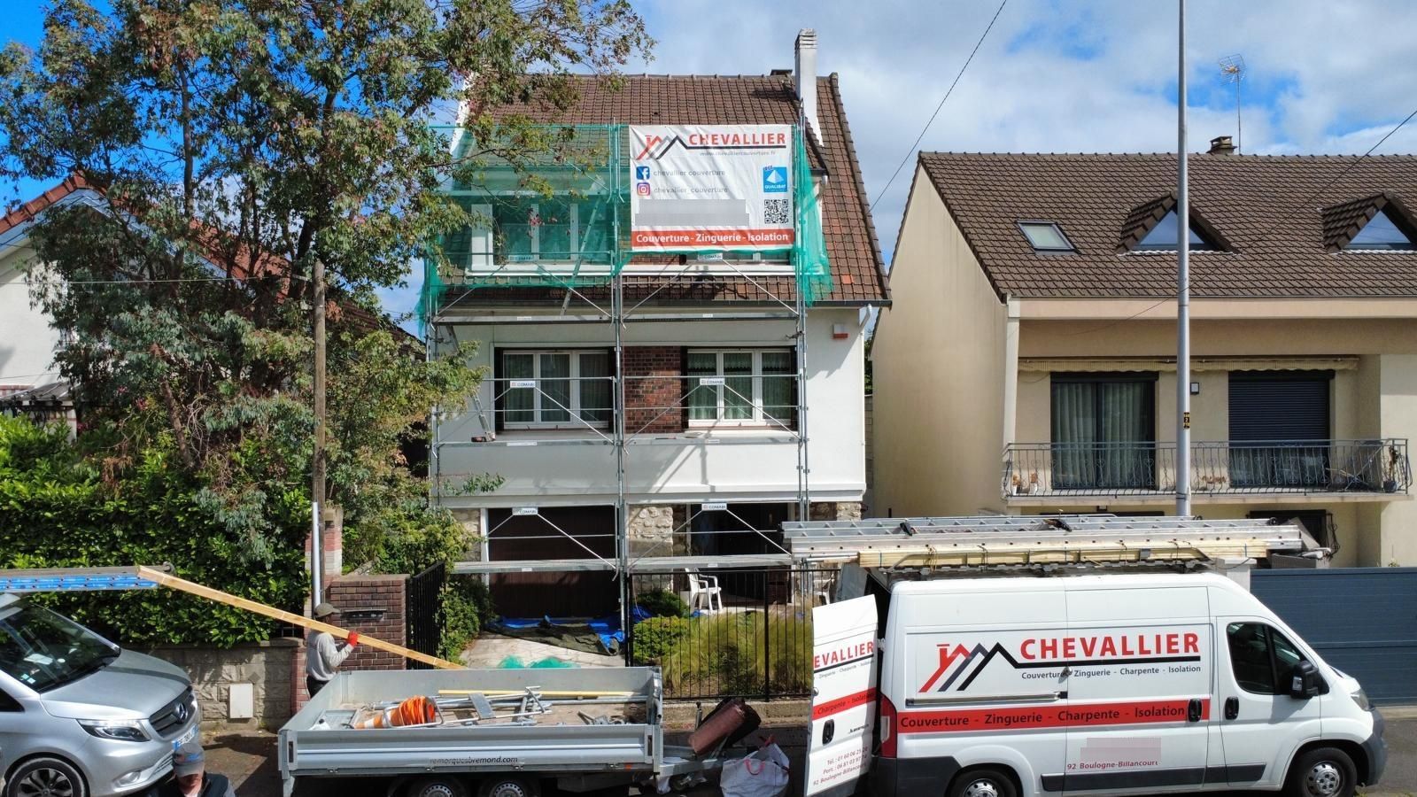 Maison à deux étages en rénovation avec échafaudages, camion de chantier et voitures garées dans une rue résidentielle.
