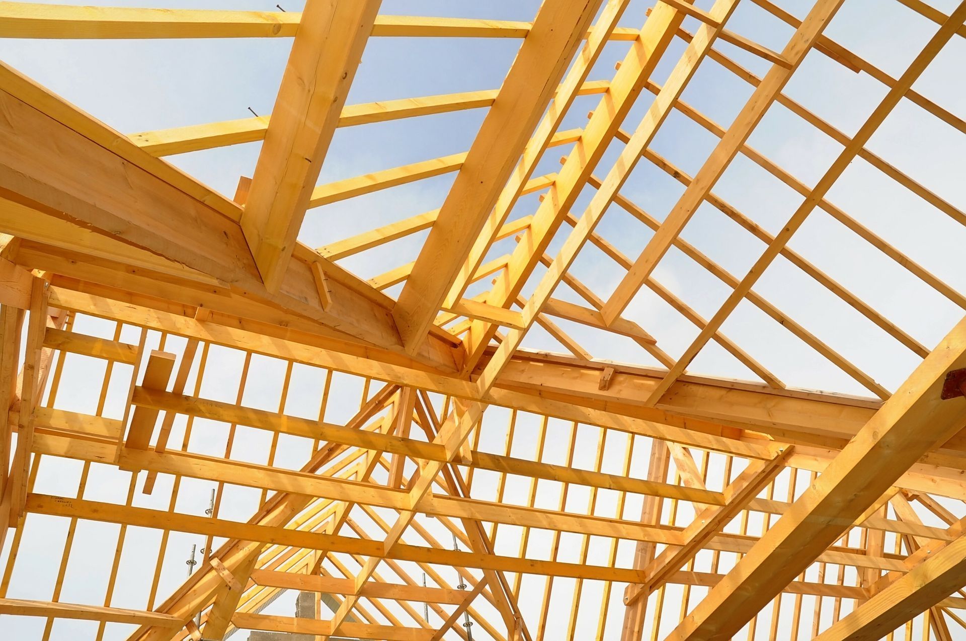 Charpente de toit en bois avec poutres et chevrons apparents en construction sur fond de ciel lumineux.