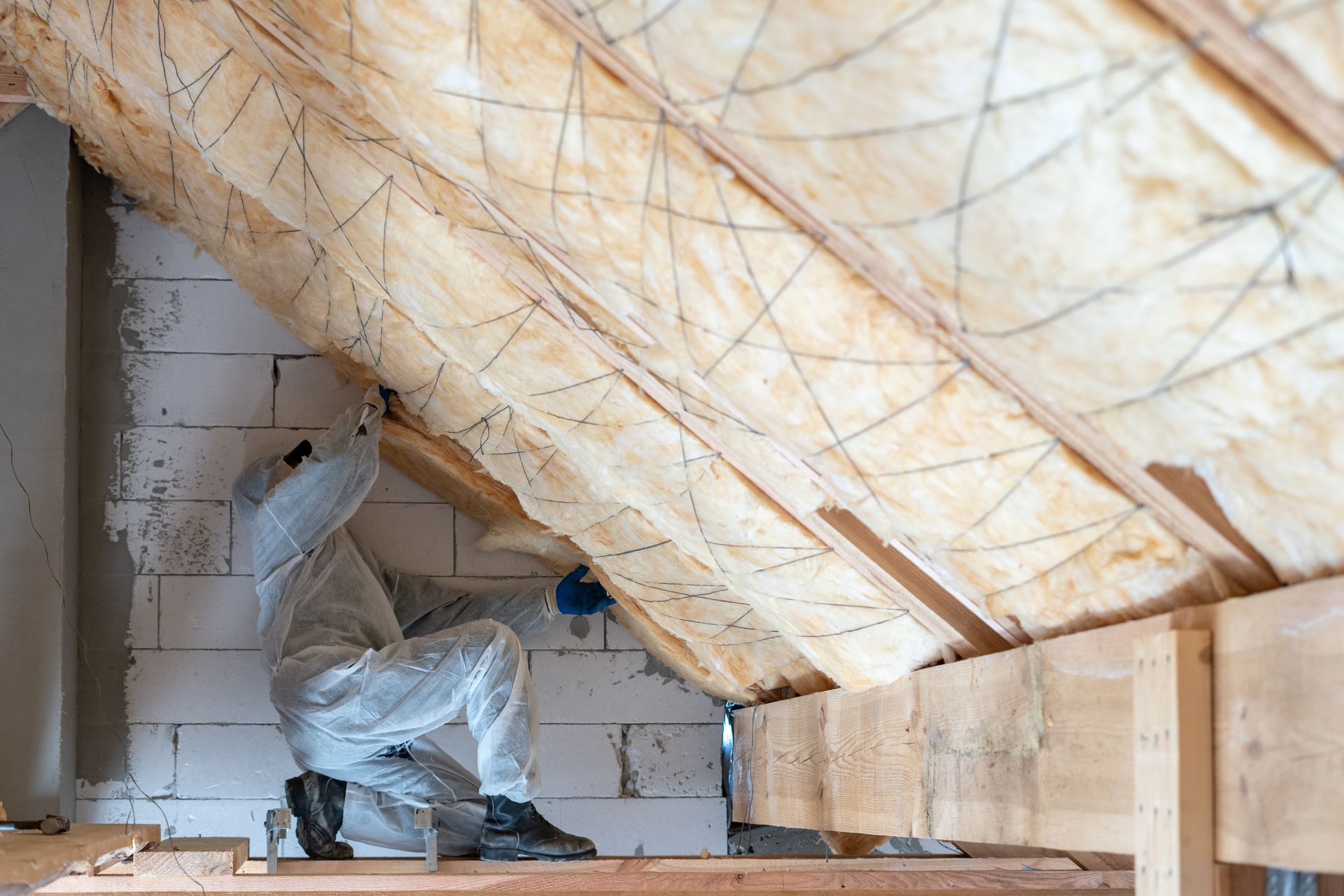 Un ouvrier en tenue de protection pulvérise de l'isolant à l'intérieur d'un grenier aux chevrons apparents.