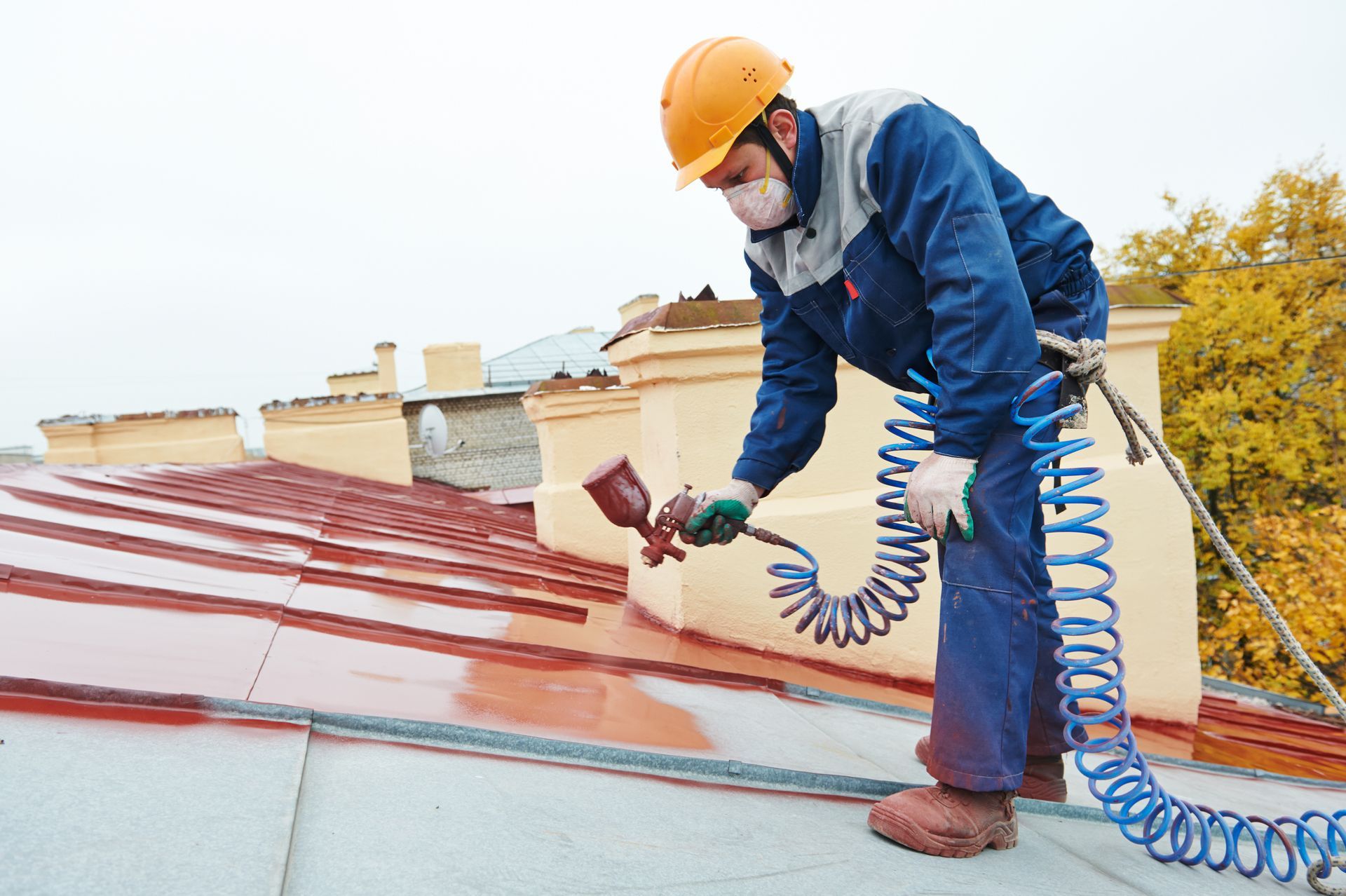 Un ouvrier portant un casque de chantier pulvérise un mastic d'étanchéité rouge sur un toit en pente.