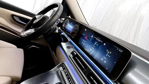 Interior de un automóvil moderno con una gran pantalla digital, volante negro y detalles en color bronce y plata.