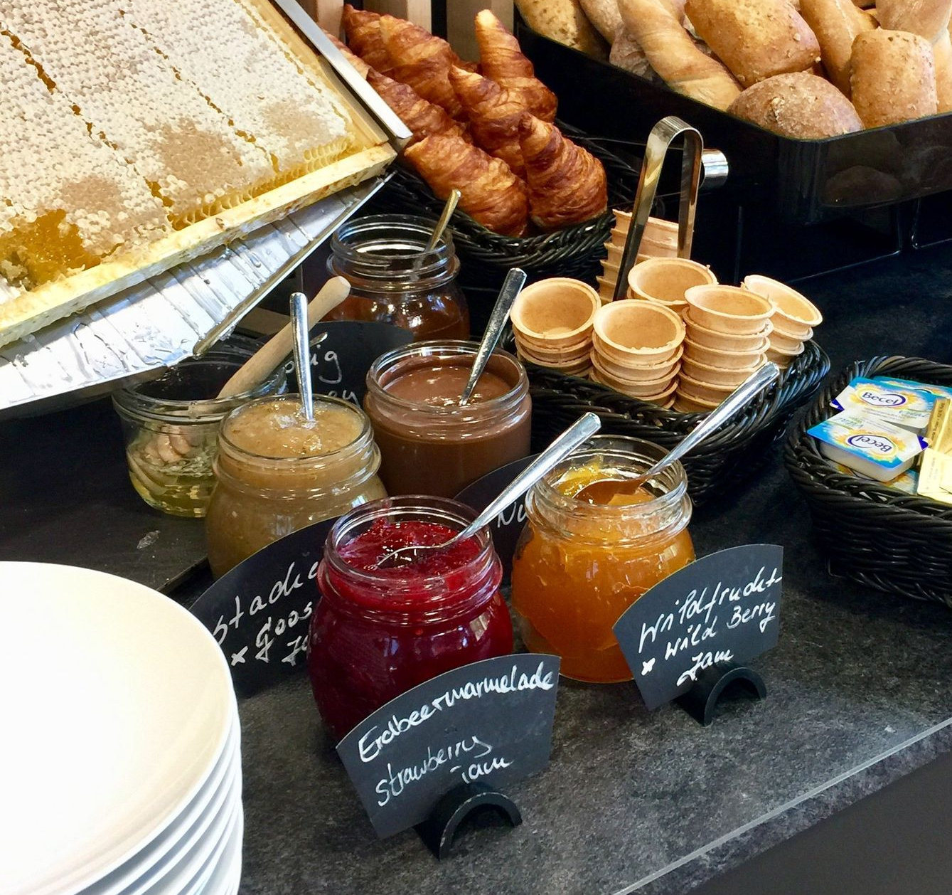 Frühstücksbuffet: Honig, Gebäck, Marmeladen im Glas, Brötchen, Waffelbecher.