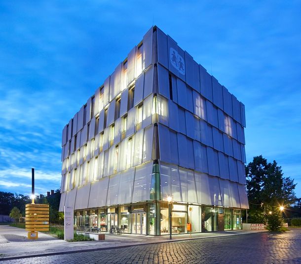 Modernes Gebäude mit geschichteter Fassade in der Abenddämmerung; Glaseingang, Kopfsteinpflasterweg.