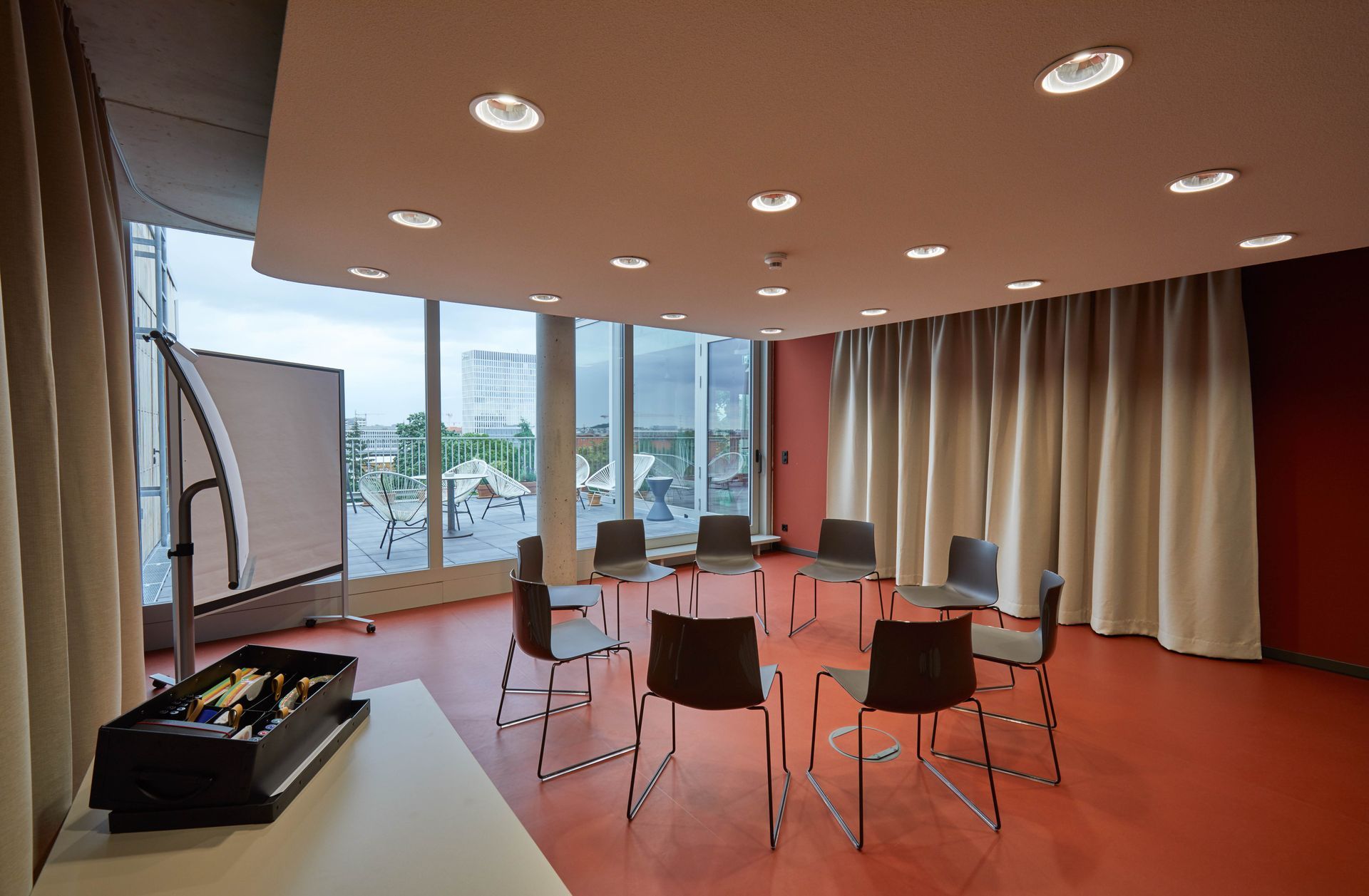 Ein runder Besprechungsraum mit im Kreis angeordneten Stühlen, einer Tafel und Fensterblick.