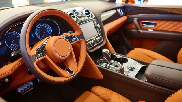 Innenraum eines Luxusautos mit Sitzen, Armaturenbrett und Lenkrad aus braunem Leder.