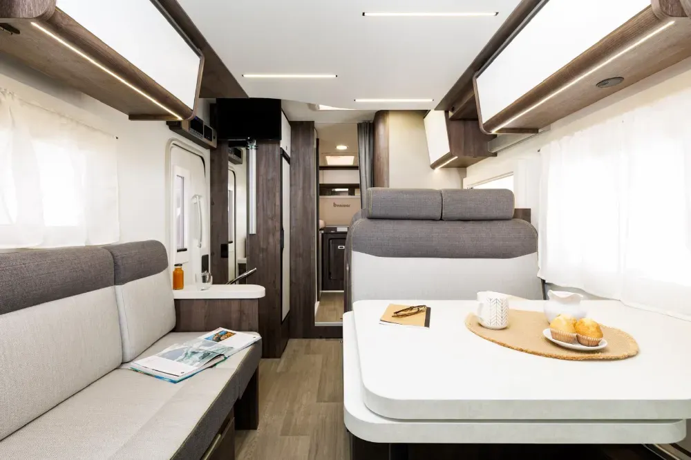 Interior de una autocaravana moderna que muestra un comedor con asientos tapizados en gris y una mesa blanca.