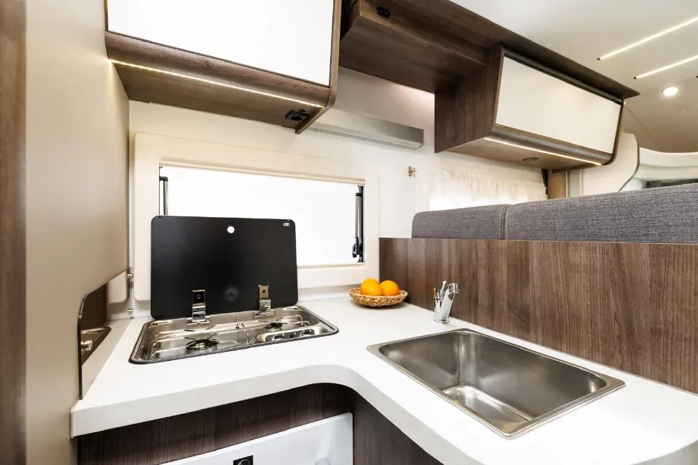 Una moderna cocina para autocaravana con encimera blanca, fregadero de acero inoxidable