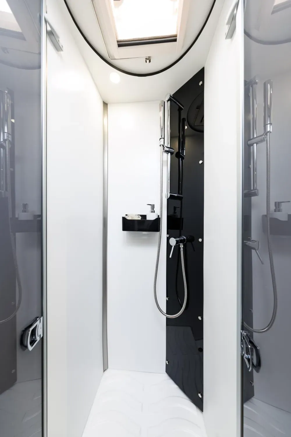 Una cabina de ducha estrecha con paredes blancas, un panel negro que contiene el cabezal de ducha cromado