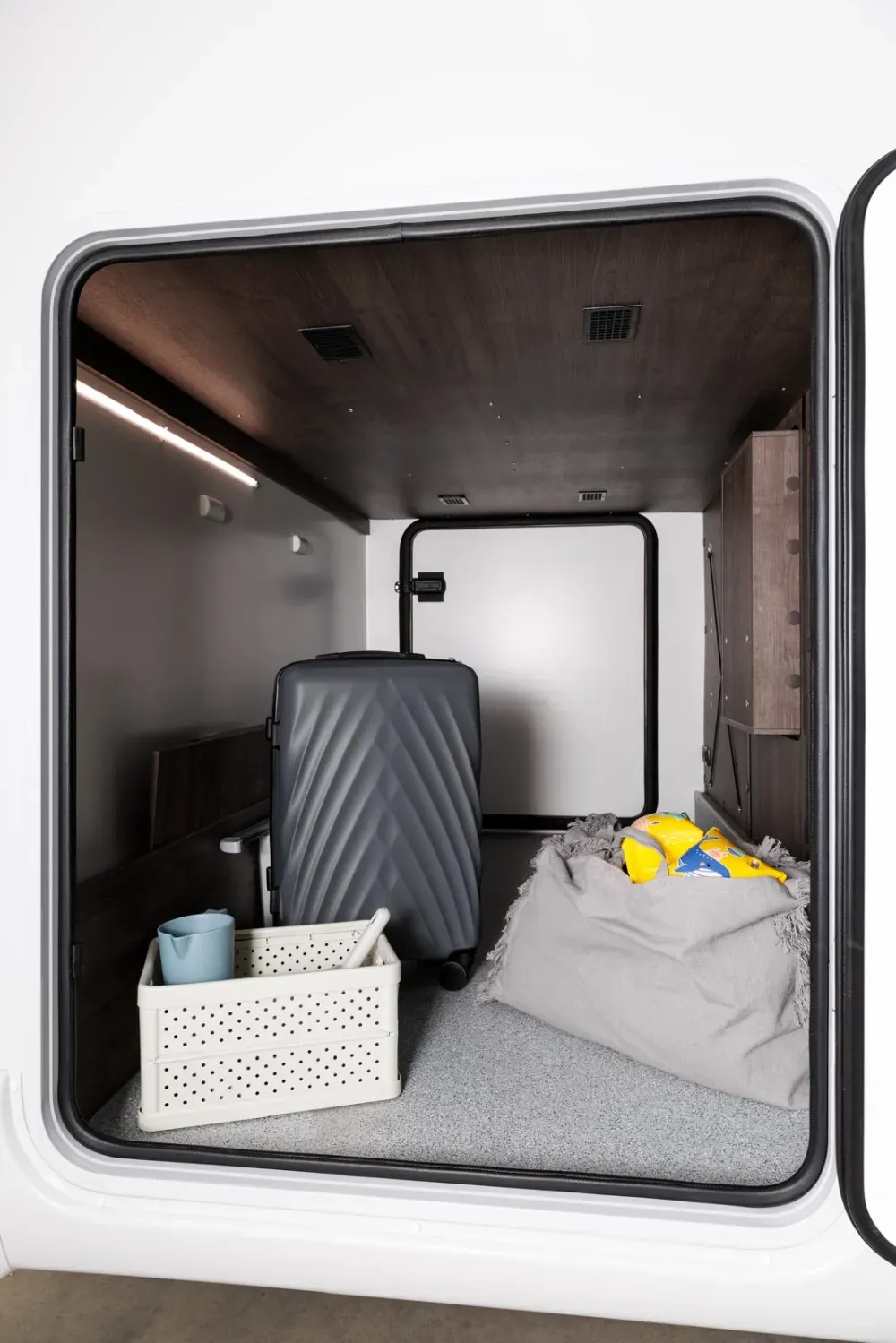 Compartimento de almacenamiento abierto de un vehículo que contiene una maleta gris,