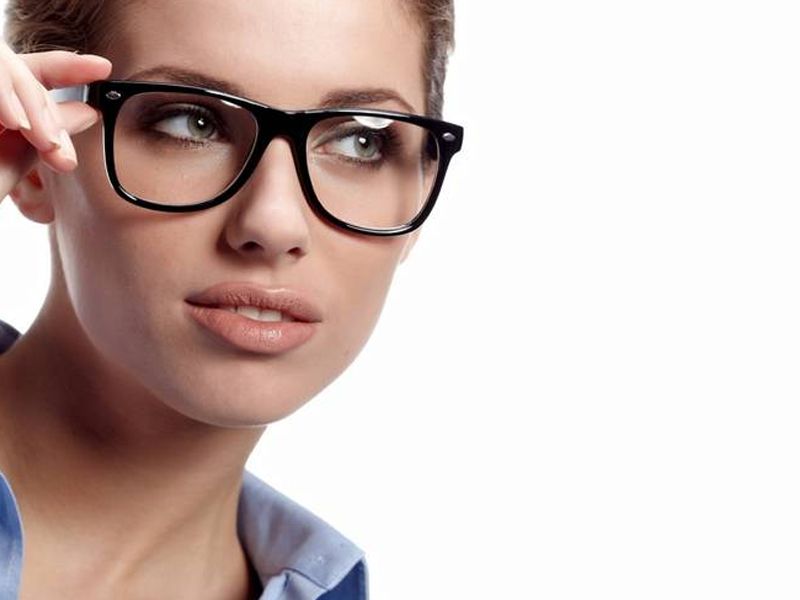 Mujer con gafas, mirada pensativa, piel clara, gafas de montura oscura y camisa azul.