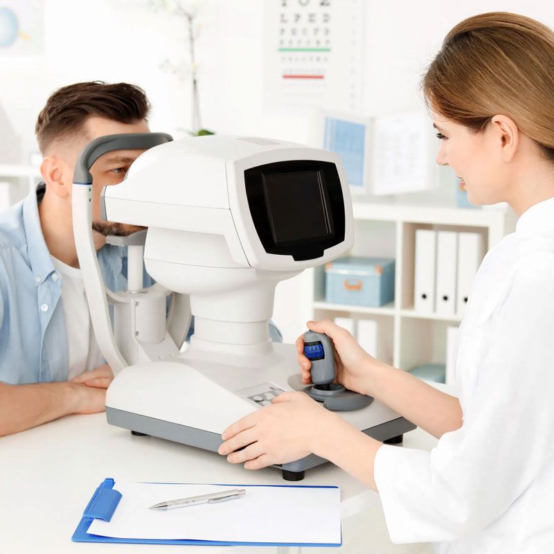 Optometrista examinando los ojos de un hombre con un autorrefractor en una oficina luminosa.