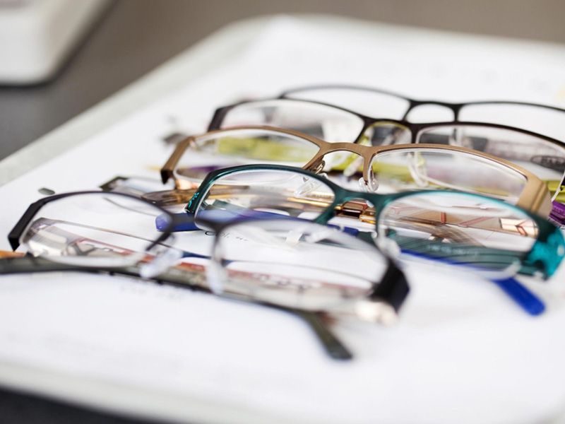 Gafas con varios colores de montura, apiladas sobre una superficie blanca.