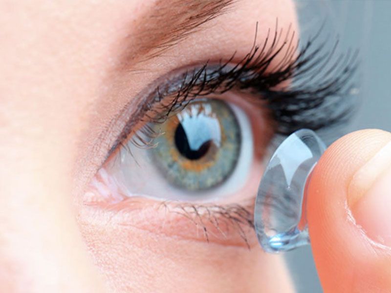 Primer plano del ojo de una persona sosteniendo una lente de contacto, preparándose para insertársela.