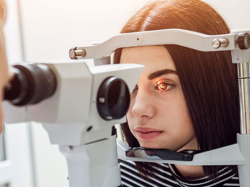 Mujer sometiéndose a un examen ocular, mirando a través de una lámpara de hendidura, con el ojo iluminado en color naranja.