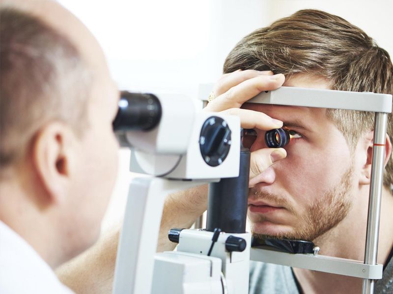 Optometrista examinando el ojo de un hombre con una lámpara de hendidura en un entorno clínico.