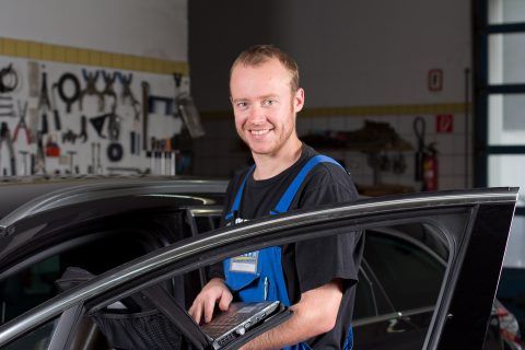 Ein Mann steht mit einem Laptop in der Hand neben einem Auto.