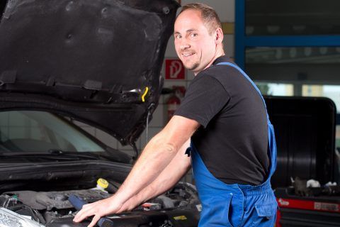 Ein Mann im blauen Overall arbeitet am Motor eines Autos.