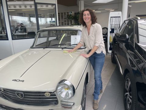 Eine Frau steht in einem Ausstellungsraum neben einem weißen Auto.