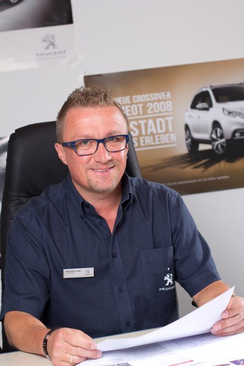 Ein Mann mit Brille sitzt an einem Schreibtisch und hält ein Stück Papier in der Hand