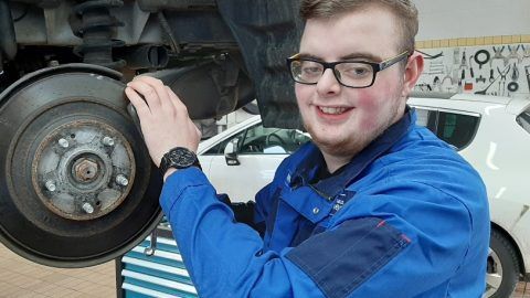 Ein junger Mann arbeitet in einer Garage an einem Auto.