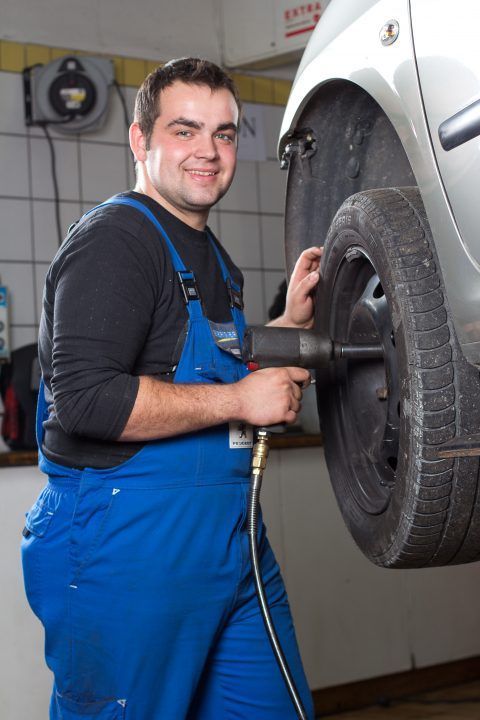 Ein Mann im blauen Overall wechselt einen Autoreifen.